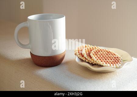 Frühstück mit Kaffee in einer weißen Tasse mit Korkboden und italienischen Waffeln auf weißem Sofa, beleuchtet vom Morgenlicht Stockfoto