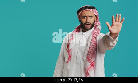 Ein Mann aus dem Nahen Osten, der mit der Hand aufhört, Negativität und Ablehnung im Studio ausdrückt. Ein junges männliches Modell, das Ablehnung zeigt, enttäuscht ist über den Hintergrund. Stockfoto