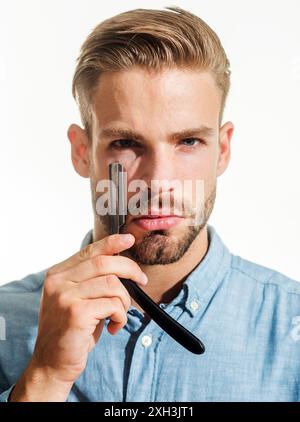 Professionelle Vintage-Friseurwerkzeuge für Friseurladen. Hübscher Friseur in stilvollem Hemd mit scharfer Klinge eines Rasiermessers. Ein bärtiger Mann, bereit zum Ssh Stockfoto