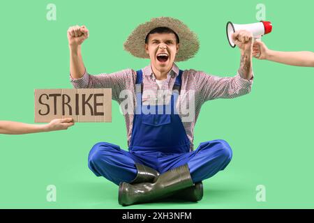 Protestierender männlicher Landwirt mit Plakat und Megaphon auf grünem Hintergrund. Schlagkonzept Stockfoto