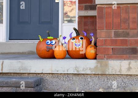 Herbsttür mit drei geschnitzten Kürbissen - verspielte Ausdrücke - saisonale Requisiten an einer Backsteinmauer. Aufgenommen in Toronto, Kanada. Stockfoto