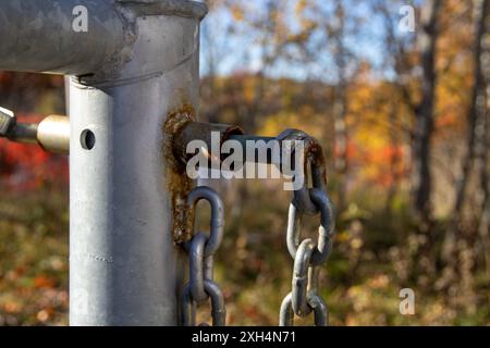 Rostiges Kettenglied am silbernen Metallständer – lebendiges Herbstlaub in weichem Hintergrund. Aufgenommen in Toronto, Kanada. Stockfoto