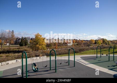 Sonniger Spielplatz - leere Schaukeln - lebhaftes Herbstlaub - klarer blauer Himmel - Freiluft-Erholungsraum in vorstädtischer Umgebung - saisonaler Wechselstube Stockfoto