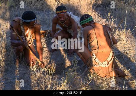 San Buschmänner beugen sich über den Boden und graben mit einem großen Stock nach Skorpionen im Busch in Botswana Stockfoto