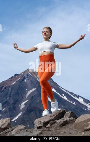 Gut proportionierte Frau mit Atemübungen, Meditation und Yoga auf dem Berg, mit einem Vulkan im Hintergrund. Yogalehrer für Erwachsene mit Stockfoto