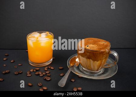 Hausgemachter Dalgona-Kaffee mit Kaffeebohnen und einem Glas Orangensaft auf Schwarz Stockfoto