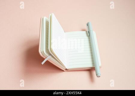 Öffnen Sie das ausgekleidete Notebook und den Stift auf rosa Schreibtischhintergrund Stockfoto