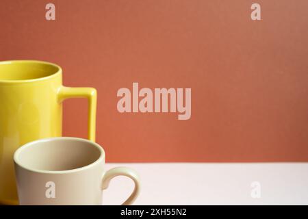 Gelbe und beige Becher auf rosa Tisch. Roter Hintergrund Stockfoto