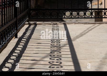 Schatten von einem kunstvollen Geländer auf einen Steinboden gegossen, wodurch interessante Formen und ein fast monochromatisches Bild entstehen. Stockfoto