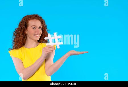 Schöne Frau in gelbem Sommerkleid, die Zeichen-Hashtag in ihrer Hand auf blauem Hintergrund mit Kopierraum hält. Soziale Medien, Blogging und virale Themen Stockfoto