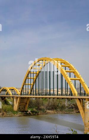 Eine gelbe Brücke überspannt einen Fluss mit einem klaren blauen Himmel im Hintergrund. Die Brücke ist ein großer Bogen und das Wasser darunter ist ruhig. Das Konzept der Tranqui Stockfoto