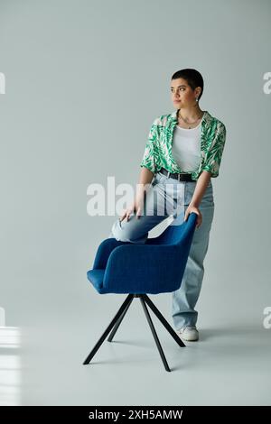 Eine junge Frau mit kurzen Haaren sitzt nachdenklich auf einem blauen Stuhl in lässiger Kleidung zu Hause. Stockfoto