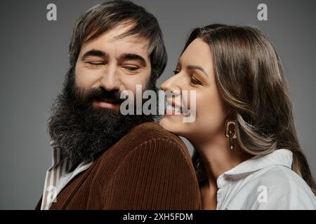 Ein liebevolles Paar in raffinierter Kleidung posiert zusammen, die Frau flüstert dem Mann ein Geheimnis ins Ohr. Stockfoto