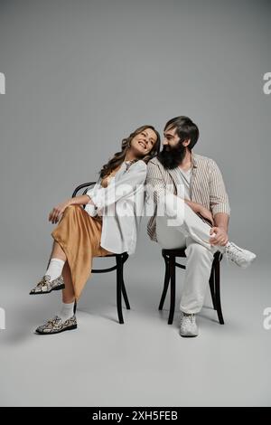 Ein Mann und eine Frau in stilvoller Kleidung sitzen auf Stühlen und schauen sich liebevoll an. Stockfoto