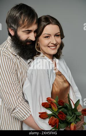 Ein Paar in eleganter Kleidung, der Mann, der die Frau nahe hält, während sie lächelt und einen Blumenstrauß hält. Stockfoto