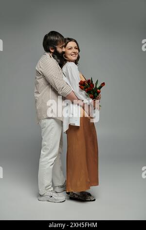Ein Paar in stilvoller Kleidung umarmt, die Frau mit einem Blumenstrauß. Stockfoto