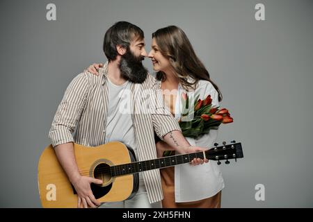 Ein Paar in raffinierter Kleidung posiert zusammen, der Mann hält eine Akustikgitarre und die Frau hält einen Strauß roter Tulpen. Stockfoto