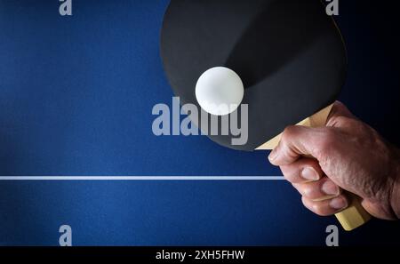 Details der Hand mit Tischtennispaddel, die einen weißen Ball auf einem blauen Spieltisch schlagen. Draufsicht. Stockfoto
