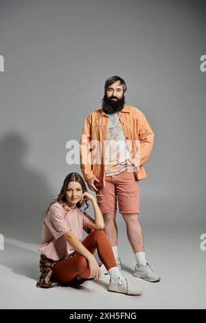 Ein stilvolles Paar posiert vor grauem Hintergrund und präsentiert seine lässige und doch elegante Kleidung. Stockfoto