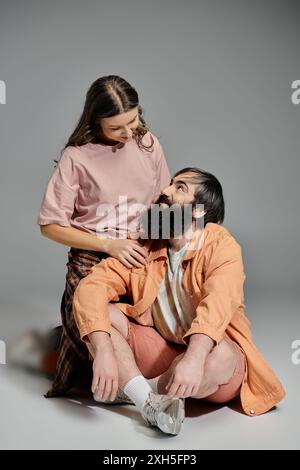 Ein Paar sitzt in einem Studio, die Frau in einem rosa Hemd und karierten Hosen, der Mann in einer orangefarbenen Jacke und Shorts, sieht sich mit Liebe an. Stockfoto