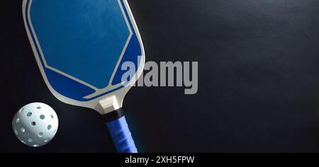 Hintergrund des blauen Pickleball-Paddels und des weißen Balls auf schwarzem Tisch. Draufsicht. Stockfoto