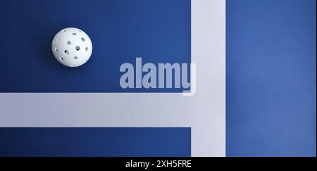 Sporthintergrund mit weißem Pickleball-Ball auf einer blauen Spielfläche mit weißen Linien. Draufsicht. Stockfoto
