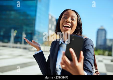 Glückliche Geschäftsfrau lacht, während sie ihr Smartphone in der Stadt hält Stockfoto