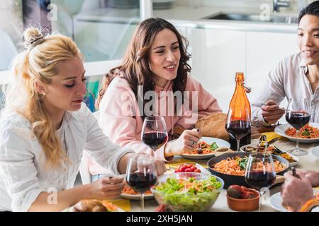 Eine Gruppe von Freunden genießt köstliche Pasta und Wein während des Mittagessens zu Hause Stockfoto
