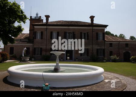 Großer weißer Brunnen, der an einem sonnigen Sommertag vor einer italienischen Villa mit grünem Rasen steht Stockfoto