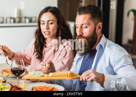 Glückliches Paar, das zu Hause eine Käseplatte und Wein zu ihrem Pasta-Abendessen genießt Stockfoto
