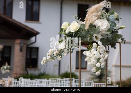 Weiße Blumen, einschließlich Rosen und Atem des Babys, werden mit Eukalyptus und Pampas Gras für eine Hochzeitszeremonie angeordnet Stockfoto