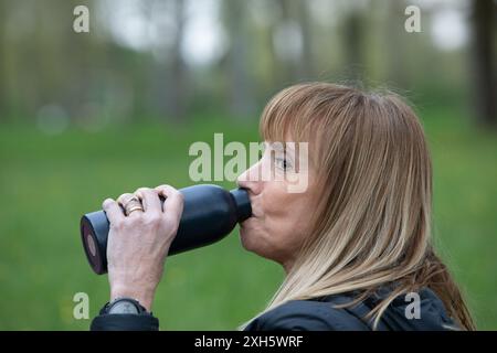Frau macht eine Pause vom Sport im Freien und genießt ein erfrischendes Getränk Wasser aus ihrer wiederverwendbaren Flasche Stockfoto