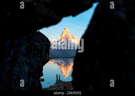 Wanderer beobachten den Sonnenaufgang über dem Matterhorn vom Stellisee aus, Blick von einer Öffnung durch Felsen, Zermatt, Wallis, Schweiz Stockfoto