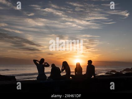 Eine Gruppe von Menschen mit Silhouette, die den Sonnenuntergang am Meer beobachten Stockfoto