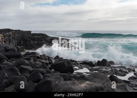 Ocean waves crash onto black lava rock along seawall in Kailua-Kona. Stockfoto