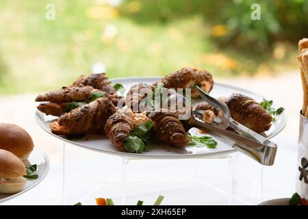 Frisch gebackene Croissants gefüllt mit Fleisch und Gemüse, serviert auf einem weißen Teller während einer Catering-Veranstaltung im Freien Stockfoto