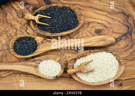 sesamum, Sesam (Sesamum indicum), geschälte und ungeschälte Sesamsamen in kleinen Holzschüsseln mit Holzlöffeln und Holzlöffeln Stockfoto
