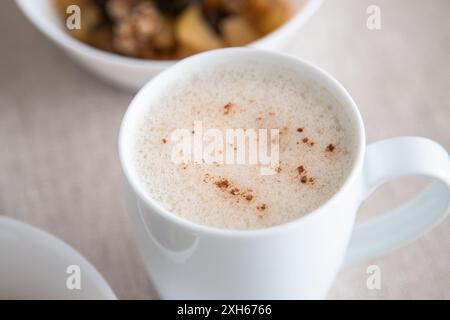 Weiße Tasse aufschäumenden Cappuccino oder Gemüsegetränk mit Zimtpulver, um ein köstliches und gesundes Frühstück zu begleiten. Stockfoto