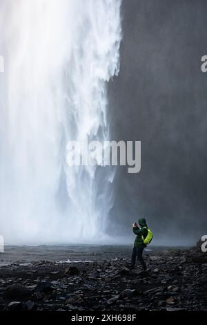 Atemberaubender Blick auf den Skógafoss-Wasserfall mit einem Touristen, der Fotos macht. Skógafoss ist einer der größten Wasserfälle in Island. Stockfoto