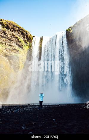 Atemberaubender Blick auf den Skógafoss-Wasserfall mit einem Touristen, der Fotos macht. Skógafoss ist einer der größten Wasserfälle in Island. Stockfoto