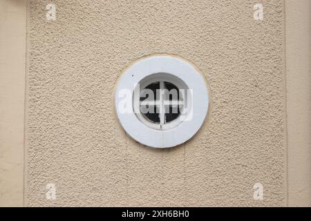 Rundes Rahmenfenster mit Holzgitter in der Mitte und Gebäudewand Stockfoto