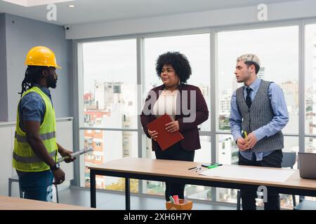 Afrikanischer Mann mit Schutzhelm und -Weste, Ingenieur, der für die Arbeit zuständig ist, kommt zum Vorstand, der sich bei Coworking trifft, er trifft sich mit Young Stockfoto