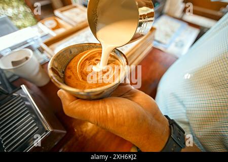 Nahaufnahme von Hand beim Ausgießen von Kaffee Latte Art. Barista Pouring Latte Art Stockfoto
