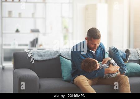 Vater, Junge und Kitzel Kind zusammen auf dem Sofa zu Hause, knüpfen und umarmen um Liebe im Gespräch. Daddy, Sohn und Familie spielen im Wohnzimmer für Spiele Stockfoto