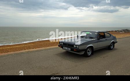 Der klassische Ford Capri in Grau und Silber wird entlang der Strandpromenade und dem Meer im Hintergrund gefahren. Stockfoto