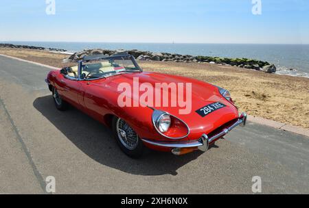 Klassischer roter Jaguar E-Type, der an der Strandpromenade am Strand und am Meer im Hintergrund geparkt wird. Stockfoto