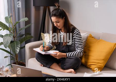 Eine junge Frau taucht in ihre Schulroutine ein, schreibt Notizen in ihr Notizbuch und verbindet Old-School-Charme mit moderner Lernatmosphäre Stockfoto