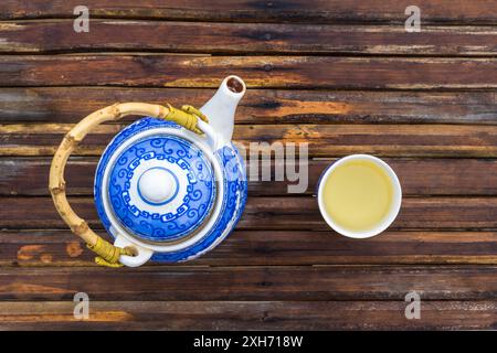 Blaue Teekanne und eine Tasse chinesischer grüner Tee auf braunem Holztisch. Draufsicht. Stockfoto