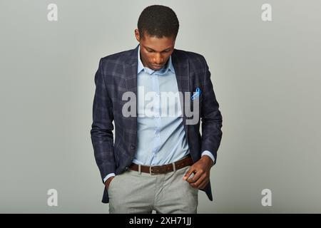 Der hübsche afroamerikanische Geschäftsmann in kariertem Blazer blickt nachdenklich nach unten. Stockfoto