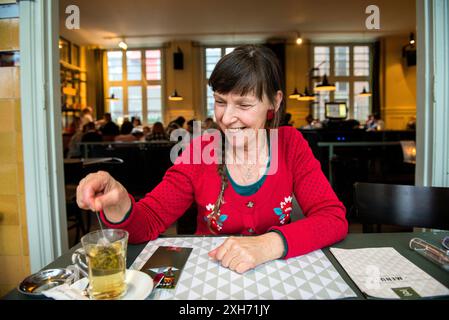 Frau in Red Senior Erwachsene, weiße Frau in roter Mode, die ihre Tasse Tee zubereitete, während sie im Restaurant Duduk Cafe auf ihr Mittagessen wartete. Tilburg, Niederlande. MRYES Tilburg Cafe Dudok Noord-Brabant Nederland Copyright: XGuidoxKoppesxPhotox Stockfoto